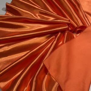 Shiny orange satin fabric with smooth, reflective surface and soft folds.